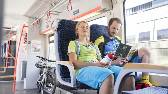Couple relaxing together inside a train traveling through St. Johann, with warm sunlight coming through the windows.