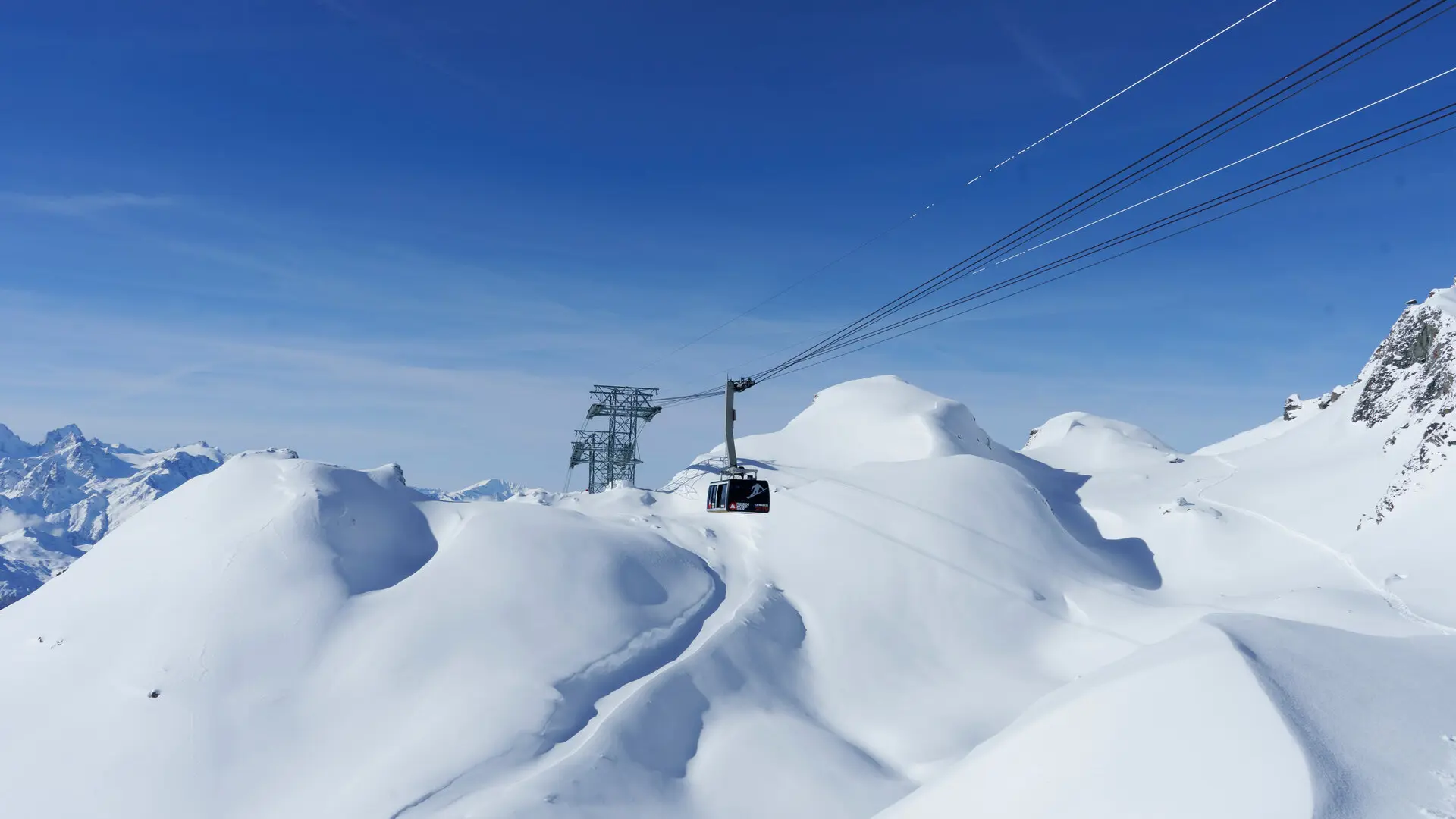 Cable car suspended above snow-covered mountains in the Four Valleys, transporting skiers across the alpine landscape.